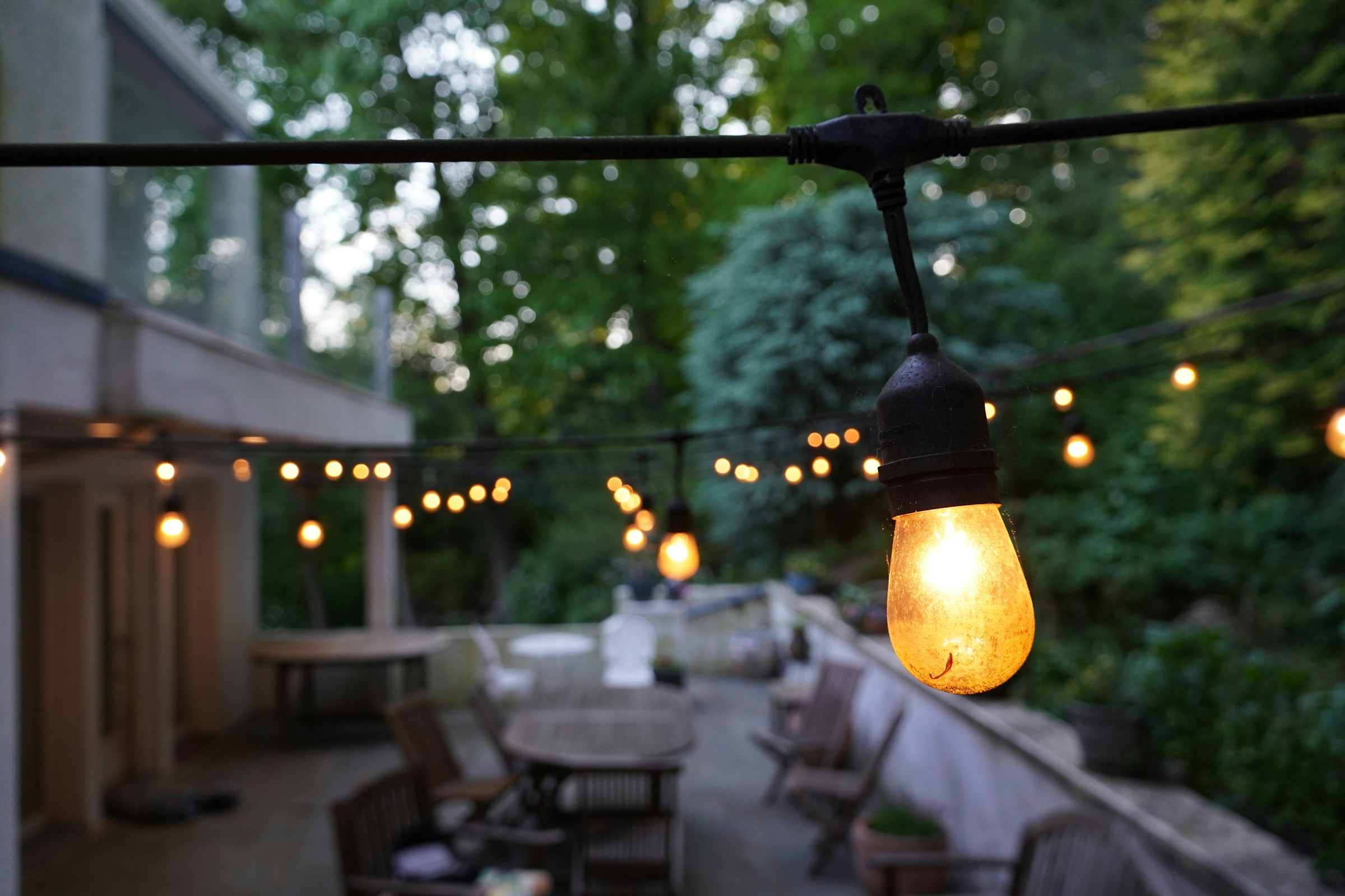 Warm string lights glowing over an outdoor patio with tables and chairs at dusk
