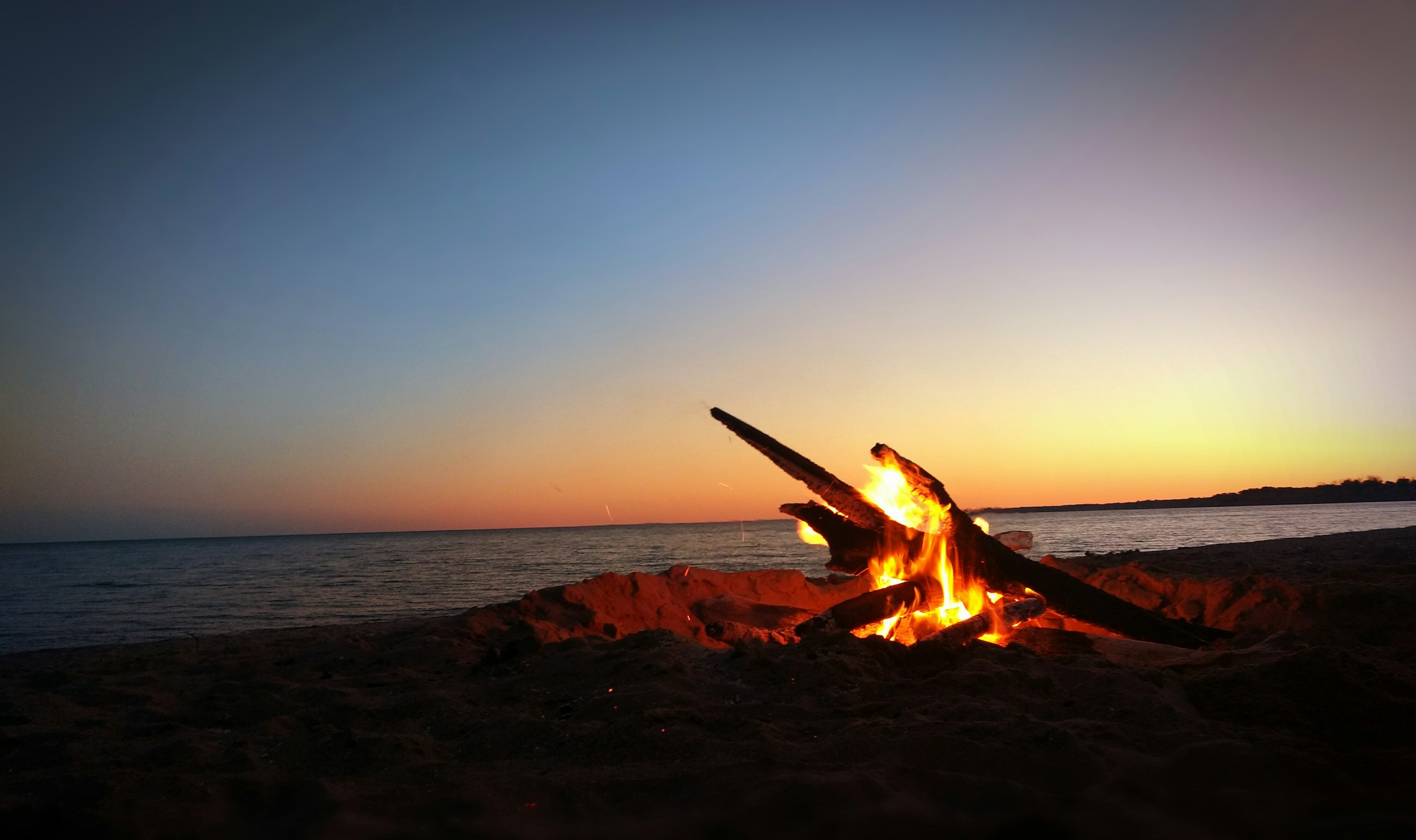 Beach bonfire burning on the sand at sunset with the ocean behind